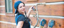 Smiling woman in blue overalls holding a garden hose.