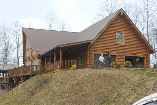 A large log home with a man standing on the porch.