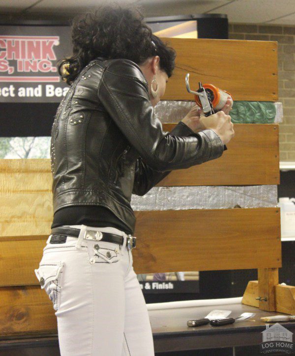 A woman in white pants and black jacket holding a gun.