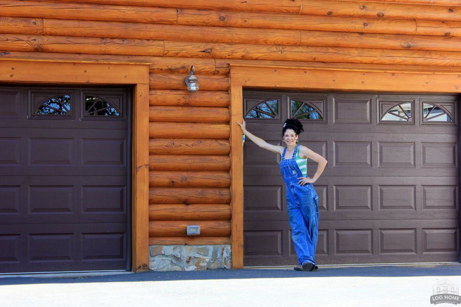 A woman in blue overalls standing next to a garage door.