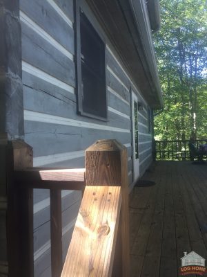 The front porch of a log cabin with a finished wooden railing.