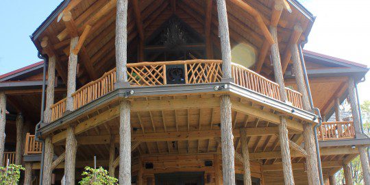 A large wooden house with a balcony and hot tub.