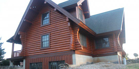 A log house with a stone wall and two windows.