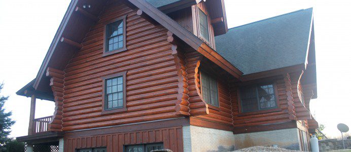 A log house with a stone wall and two windows.