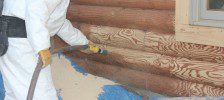 A person in white suit painting logs on the side of a house.